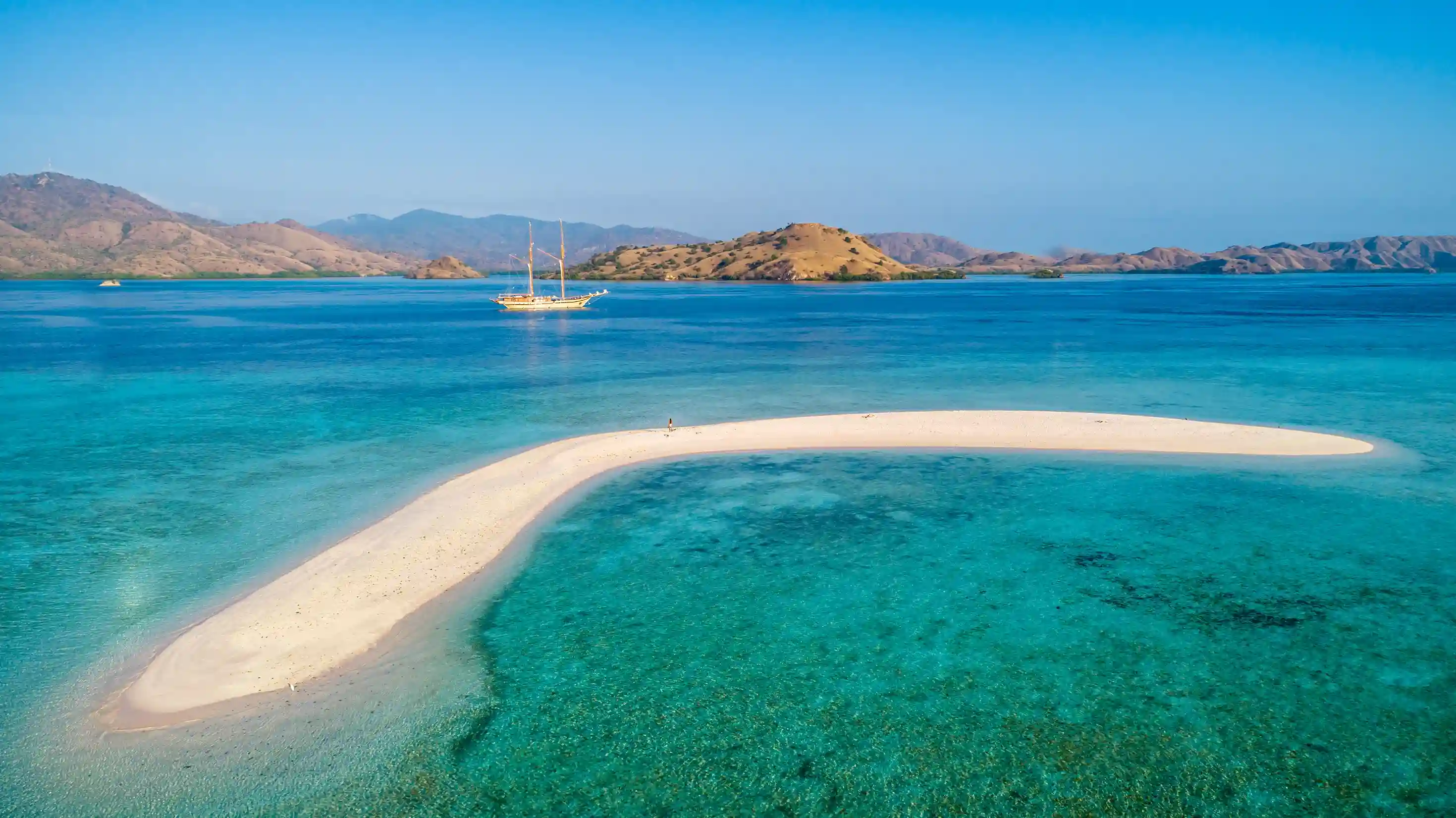 Crescent sandbar in vivid turquoise shallows under clear sky