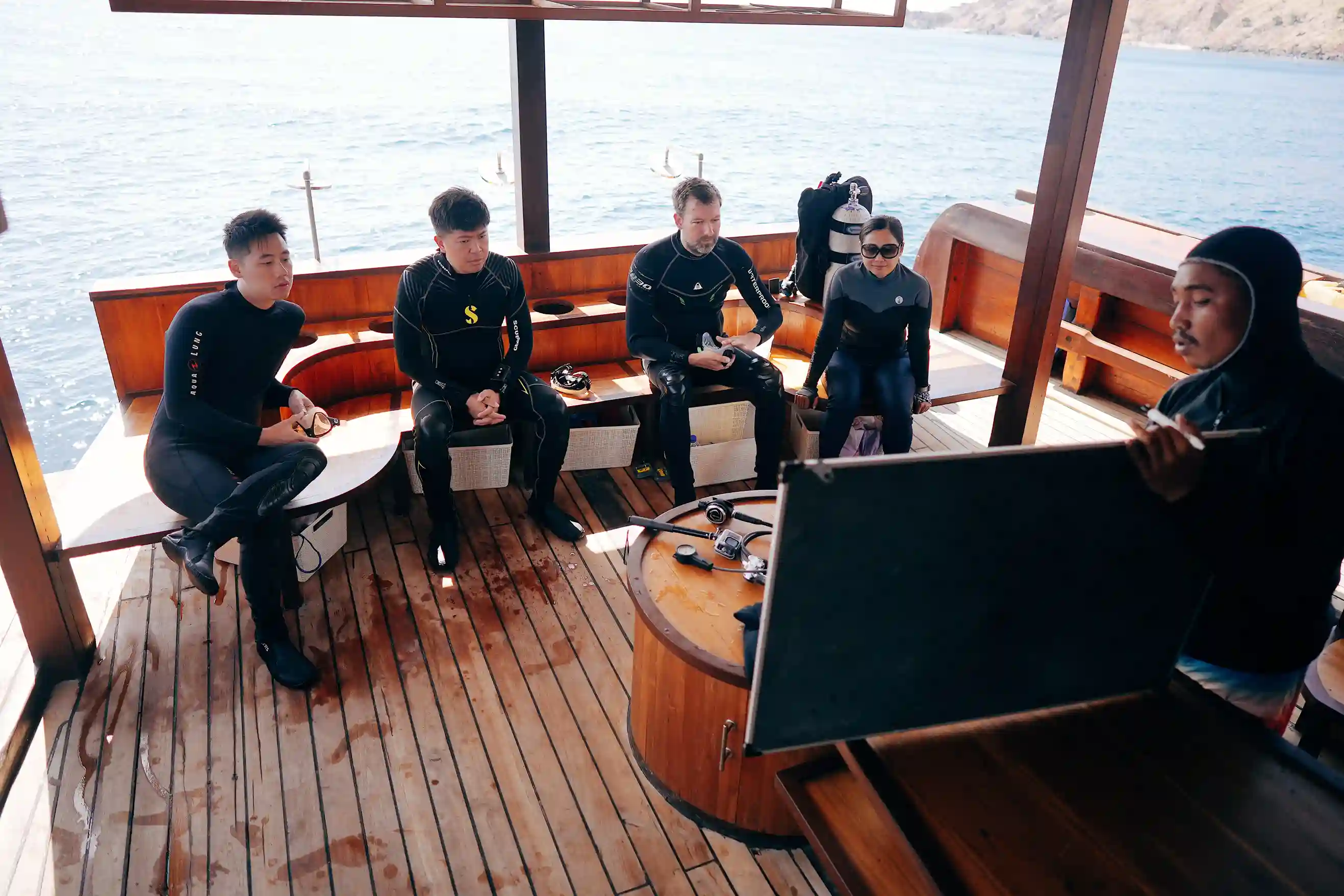 Divers in wetsuits preparing on the teak dive deck of a boat