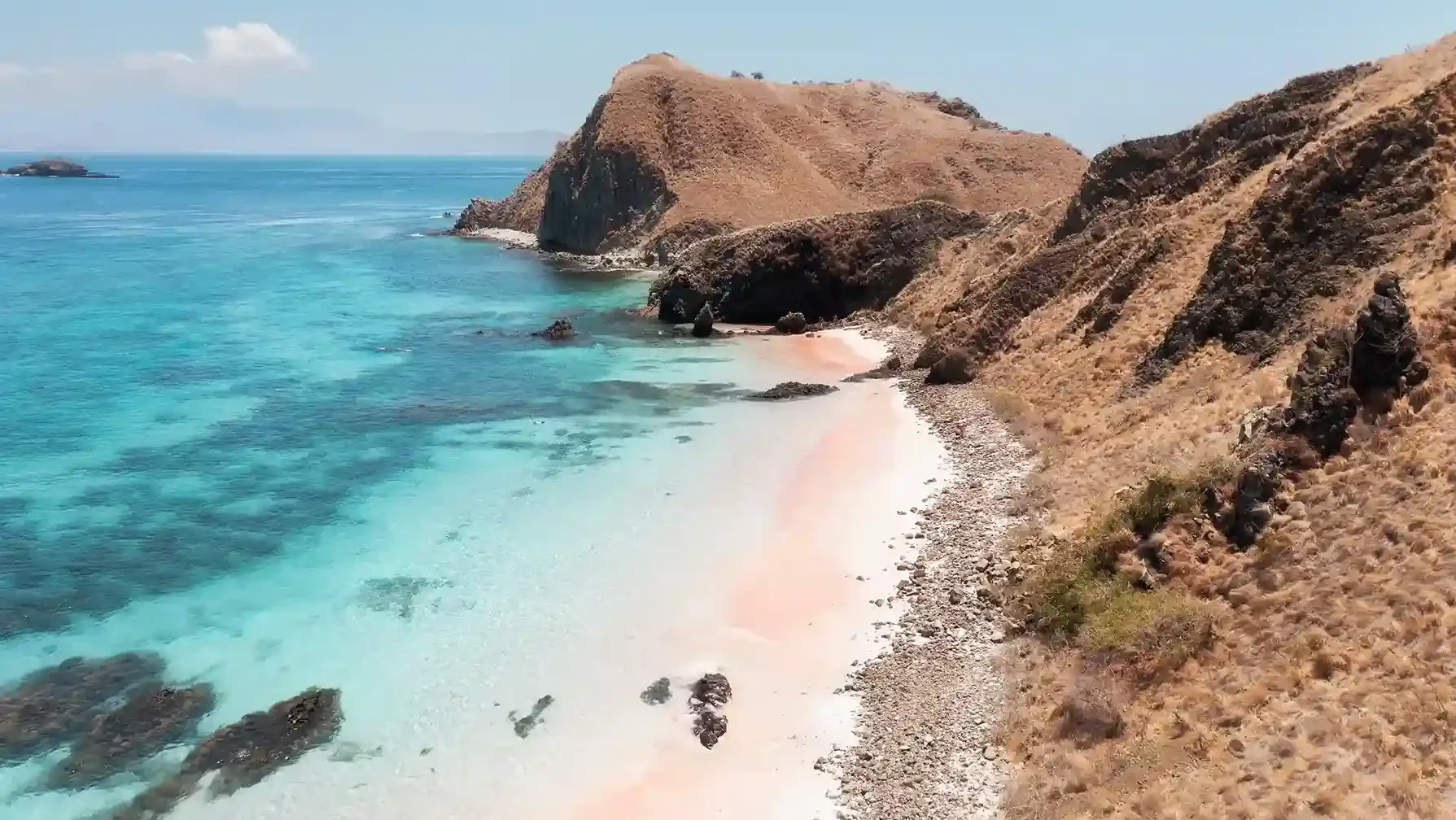 Pink-tinged beach curving into clear turquoise shallows